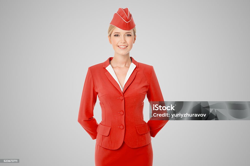 Charming Stewardess Dressed In Red Uniform On Gray Background. Cabin Crew Stock Photo