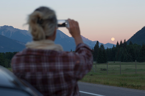 Woman takes picture of moonrise with smart phone, mountains