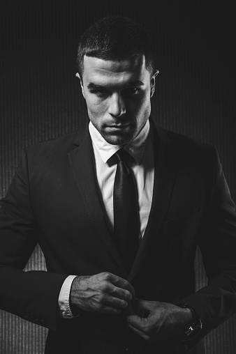 Black and white portrait of a stylish young man in a black suit. Studio shoot.
