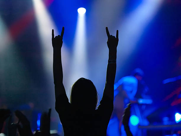 Girl raising up hands on rock concert Silhouette of girl on rock concert raised up hands with rock-n-roll gesture with blue stage and spotlights in the background heavy metal stock pictures, royalty-free photos & images