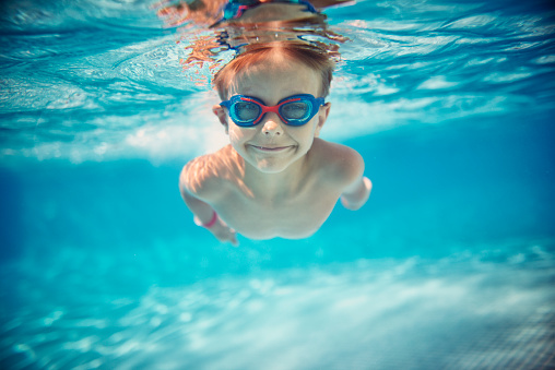Portrait of smiling little boy enjoying underwater swim in the pool towards the camera. Sunny summer day.