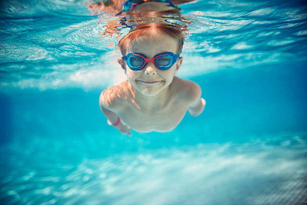 Little boy swimming underwater in pool Portrait of smiling little boy enjoying underwater swim in the pool towards the camera. Sunny summer day. swimming goggles stock pictures, royalty-free photos & images