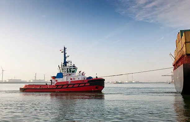 full length shot of a tugboat towing cargo container ship in Rotterdam harbour