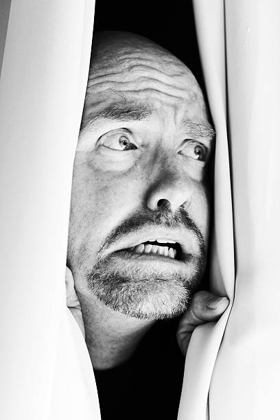 istock Terrified mature man sees something awful from behind curtains 523696915