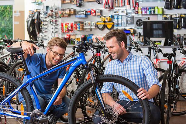 Man buying bicycle in sport store Man buying a bicycle in bike store, talking with shop assistant and watching the mountain bike together. bicycle shop stock pictures, royalty-free photos & images