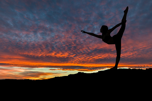 Silhouette of woman dancing and exercising on mountain top with sunset sky in the background. Copy space.