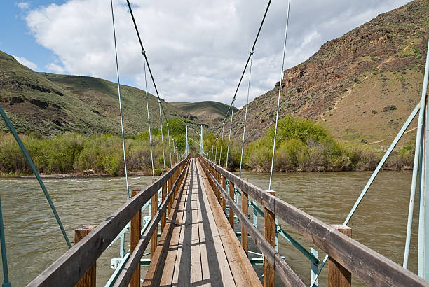 Footbridge Over the Yakima River East of the Cascade Mountains, Washington’s climate is arid and the terrain is desert-like. Summertime temperatures can exceed 100 degrees Fahrenheit in regions such as the Yakima Valley and the Columbia River Plateau. This is an area of rolling hills and flatlands. During the last Ice Age, 18,000 to 13,000 years ago, floods flowed across this land, causing massive erosion and leaving carved basalt canyons, waterfalls and coulees known as the Channeled Scablands. This scene of the Yakima River was photographed from Umtanum Creek Canyon in the L. T. Murray State Wildlife Recreation Area between Ellensburg and Yakima, Washington State, USA. jeff goulden washington state desert stock pictures, royalty-free photos & images