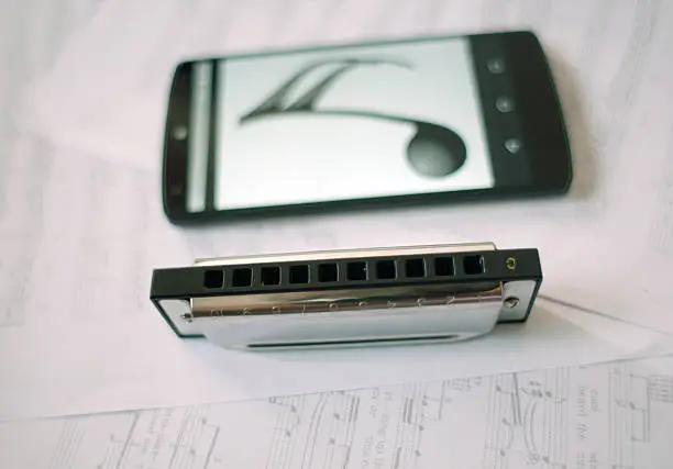Harmonica and phone with musical not laying on  musical note.