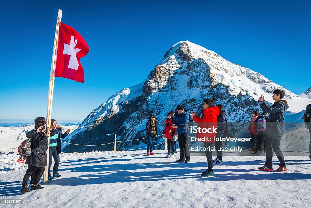 Switzerland Japanese tourists beside Swiss flag on mountain Jungfrau Alps Kleine Scheidegg, Switzerland - 24th February 2014: Group of Japanese tourists enjoying the bright sunshine and winter snow on the Jungfraujoch pass at the top of the Eiger railway high in the Alps of the Bernese Oberland, Switzerland. Beauty In Nature Stock Photo