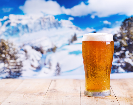glass of beer on wooden table over winter landscape