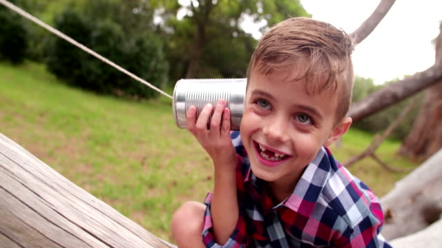 Cute little Boy curiously listening on tin can phone in park