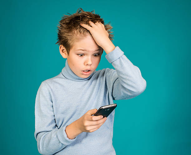 Surprised boy playing games on smartphone on blue background.