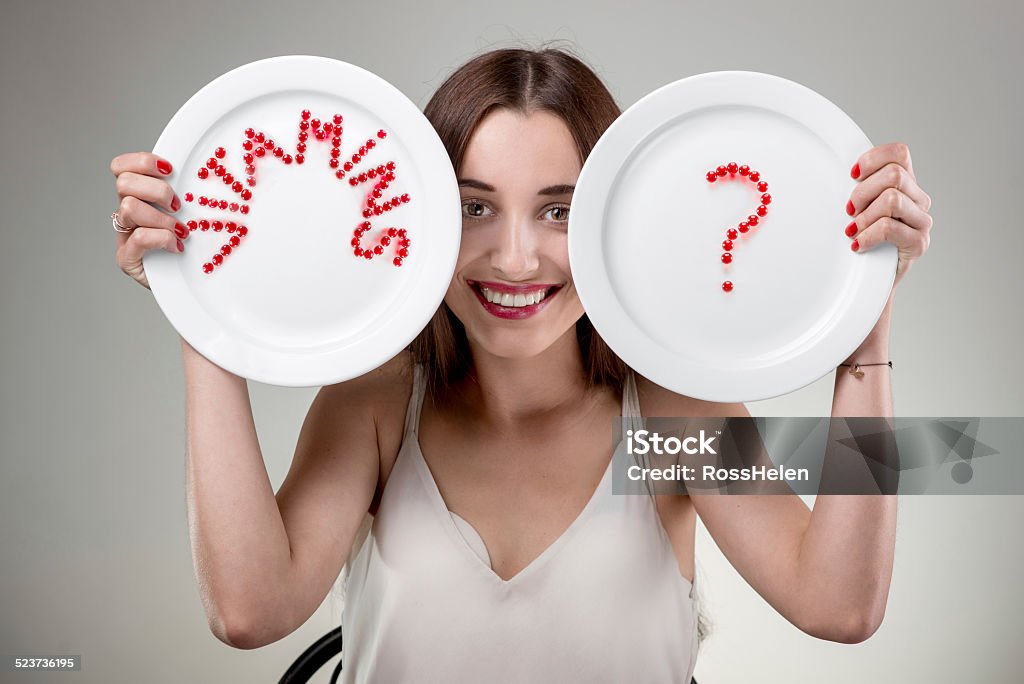 Young woman showing plates. Young woman showing plate with vitamins pills set out the word vitamins in studio on white background Adult Stock Photo