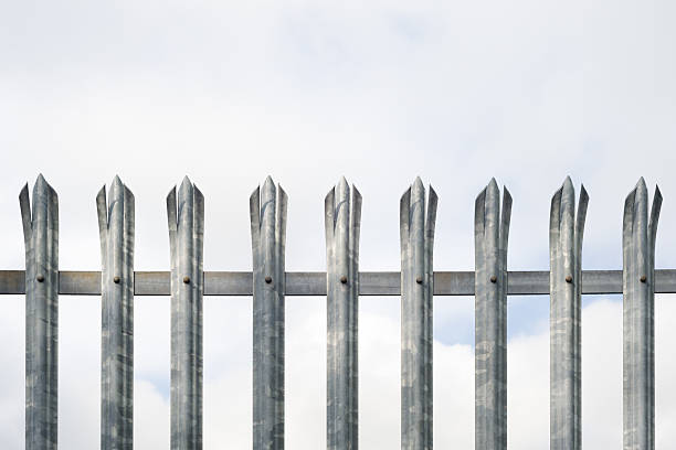 Close-up of a triple pointed, galvanised steel fence shot against an overcast sky. Excellent detail in the fence.