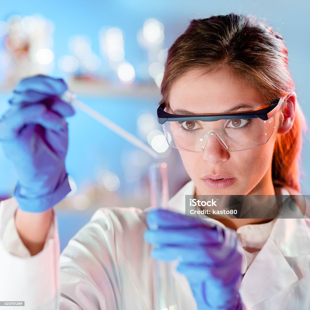 Attractive young scientist pipetting. Focused young life science professional pipetting solution into the glass cuvette. Lens focus on the researcher's eye. Laboratory Stock Photo