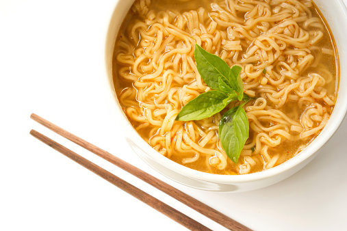 Instant noodle with basil leaf in a white bowl. On whit background and chopsticks on background.