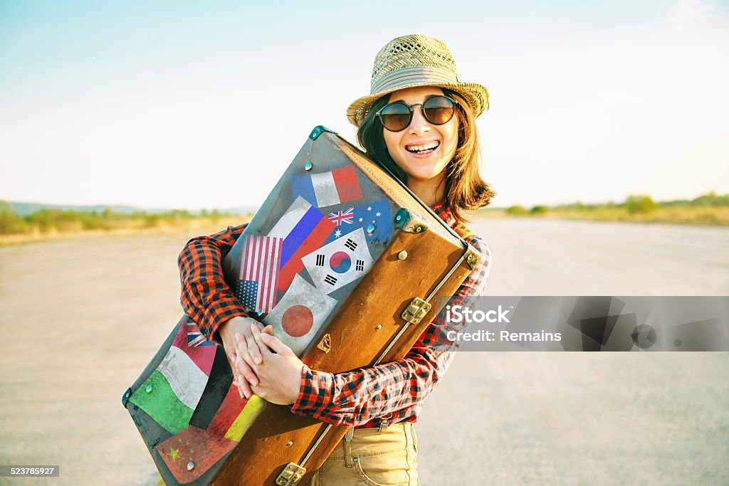 Woman embraces a suitcase with stamps flags Happy woman traveler embraces a vintage suitcase on road. Suitcase with stamps flags representing each country traveled. Label Stock Photo