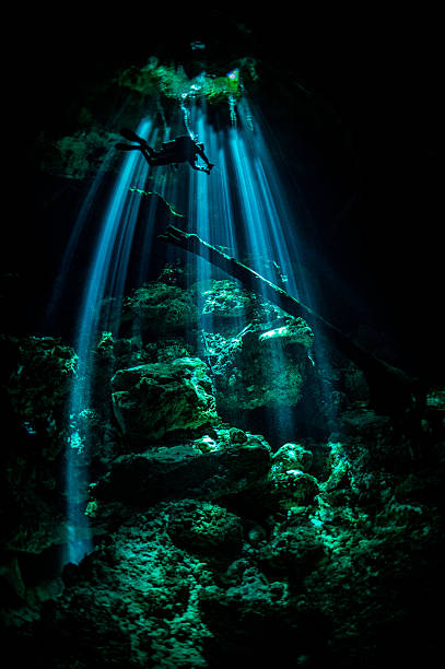 Scuba diver descending in dark cave Scuba diver exploring the underwater cenotes in Mexico near Puerto Aventuras. Caves are dark and the light always gives different amazing ambient underwater. puerto aventuras stock pictures, royalty-free photos & images