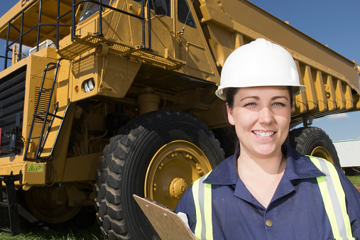 A royatly free image from industry, either construction, oil and gas or mining, of a female worker in front of a hauling truck.