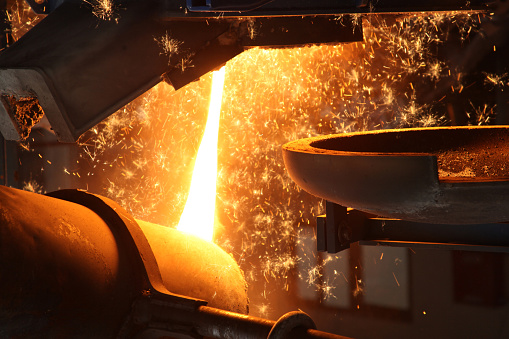 Molten metal and bronze are poured into mold by melter in a foundry plant.