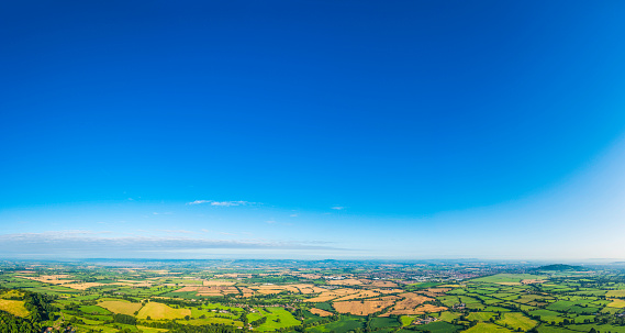 Big blue summer skies over picturesque patchwork landscape of green pasture and golden crop fields, rural villages, farms and country towns. ProPhoto RGB profile for maximum color fidelity and gamut.