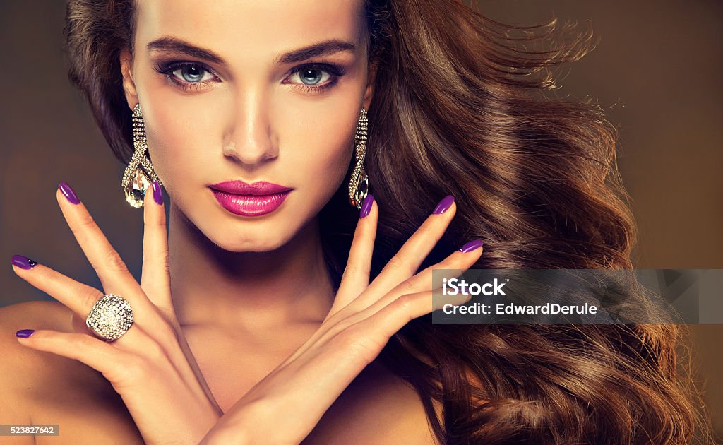 Luxury fashion style.Brunette with long curled hair. Beautiful model brunette with long curled hair. Luxury fashion style, nails manicure, cosmetics, make-up and brilliant jewelry.  Jewelry Stock Photo