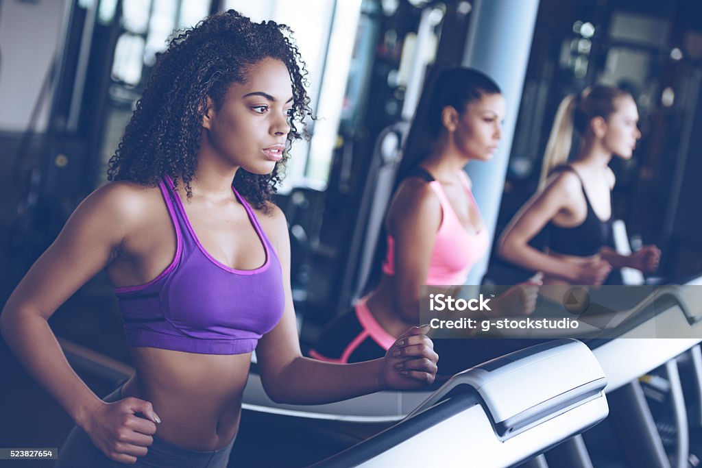 Running together. Side view close up of young beautiful women looking away while running on treadmill at gym Treadmill Stock Photo