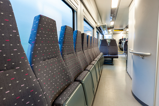 Interior of a modern and clean train car. The train car is empty and the seats are blue with red polka dots. The seats are arranged in rows and the aisle is in the center. The train car is well-lit and the windows are on the left side of the image.