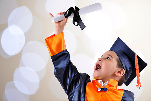 Elementary boy proudly wearing his graduation cap and gown over bokeh background.
