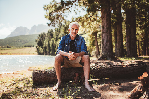 Portrait of relaxed mature man sitting on a wooden log near the lake. Mature man enjoying a day at the lake.