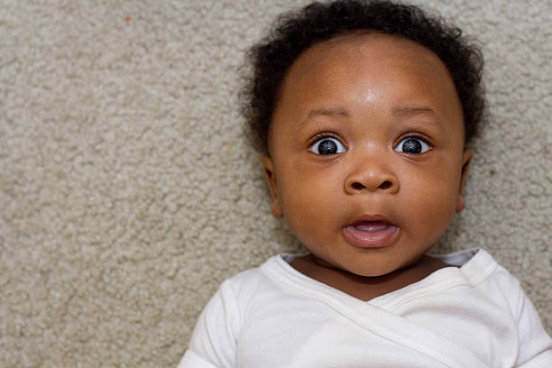 Black baby laying down looking at camera African American boy (6 months old) laying on his back looking up at the camera surprised with eyes open wide. cute black babys stock pictures, royalty-free photos & images