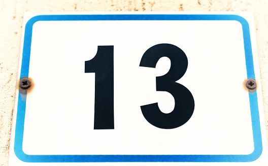 A vintage white and blue number 13 street address, set with rusty screws (close-up).