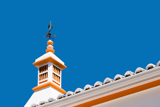 Portugese rooftop chimney Traditional Portugese rooftop chimney topped with a compass rose and rooster against a clear blue sky. alte algarve stock pictures, royalty-free photos & images
