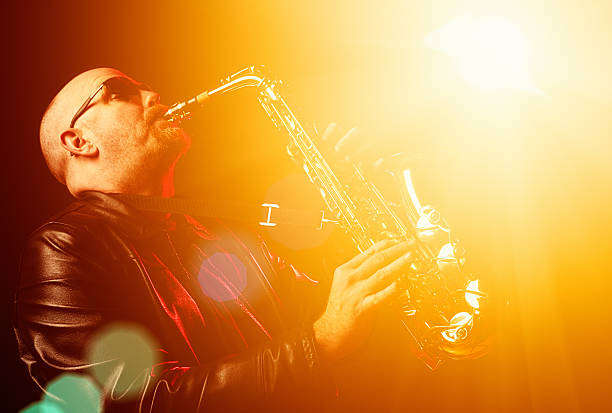 Saxophonist playing with passion at club Saxophonist looks intense as he blows his horn under bright stage lights. big band jazz stock pictures, royalty-free photos & images