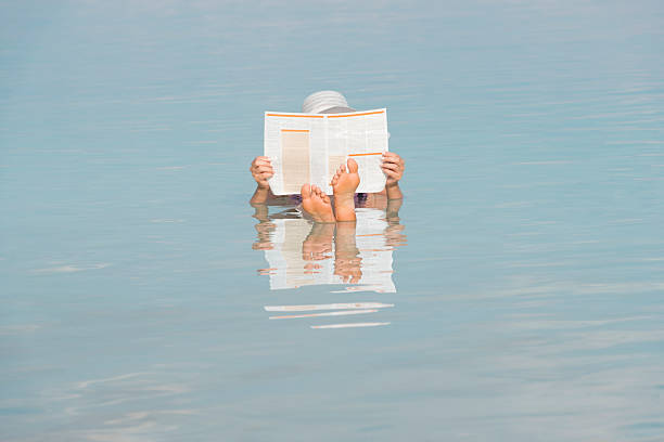 mujer leyendo el periódico mientras flota en el mar muerto. - mujer leyendo periodico fotografías e imágenes de stock