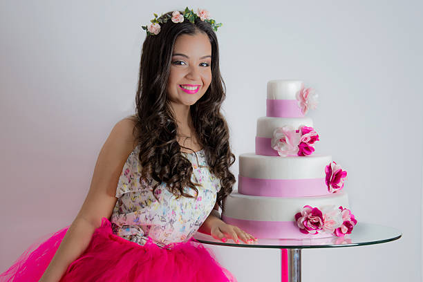 beautiful young girl 15 years in test debutante posing next to the 4-storey cake, decorated with flowers in shades of white and pink