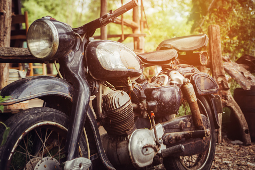 An old motorcycle parked in countryside next to wooden barn