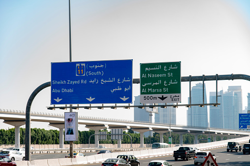 A street name plate, in English and Arabic, in the district of Jabal Amman in the capital of Jordan.  In Arabic it identifies a particular sub-district of Jabal Amman. Plates in this style appear on walls throughout the city.  In the background is the Inter-Continental Hotel (left) and a high-rise building (right).   This image was taken on a sunny afternoon on 21 April 2023.