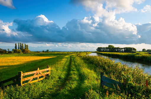 Small curved dyke along a canal with a nice cloudy sky above. Typical Dutch landscape near Schermerhorn, Netherlands.