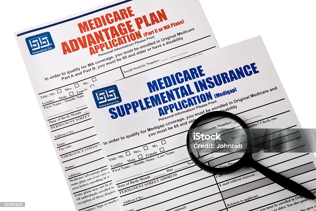 Medicare Applications, magnifying glass on top, Isolated on white Blank Medicare Applications for both Medicare Supplemental Insurance and Medicare Advantage Plan, magnifying  glass on top of applications. Isolated on white. Image shot with Canon 5D Mark2, 100 ISO, 24-115mm lens, and studio strobes. Application Form Stock Photo