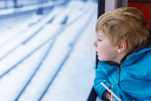 Adorable little kid looking out train window outside, while it moving. Going on vacations and traveling by railway in winter.