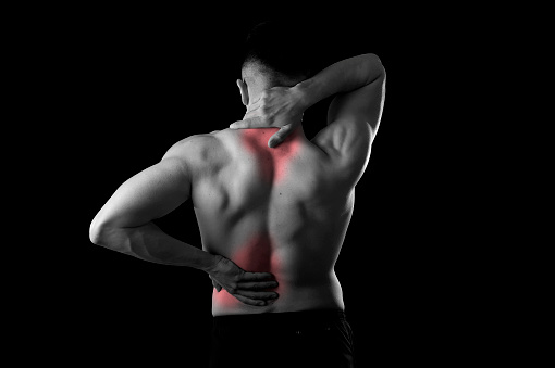 back view of young man with muscular body holding his neck and low back suffering pain in sport spinal injury and fitness stress isolated on black and white with red spot sore area