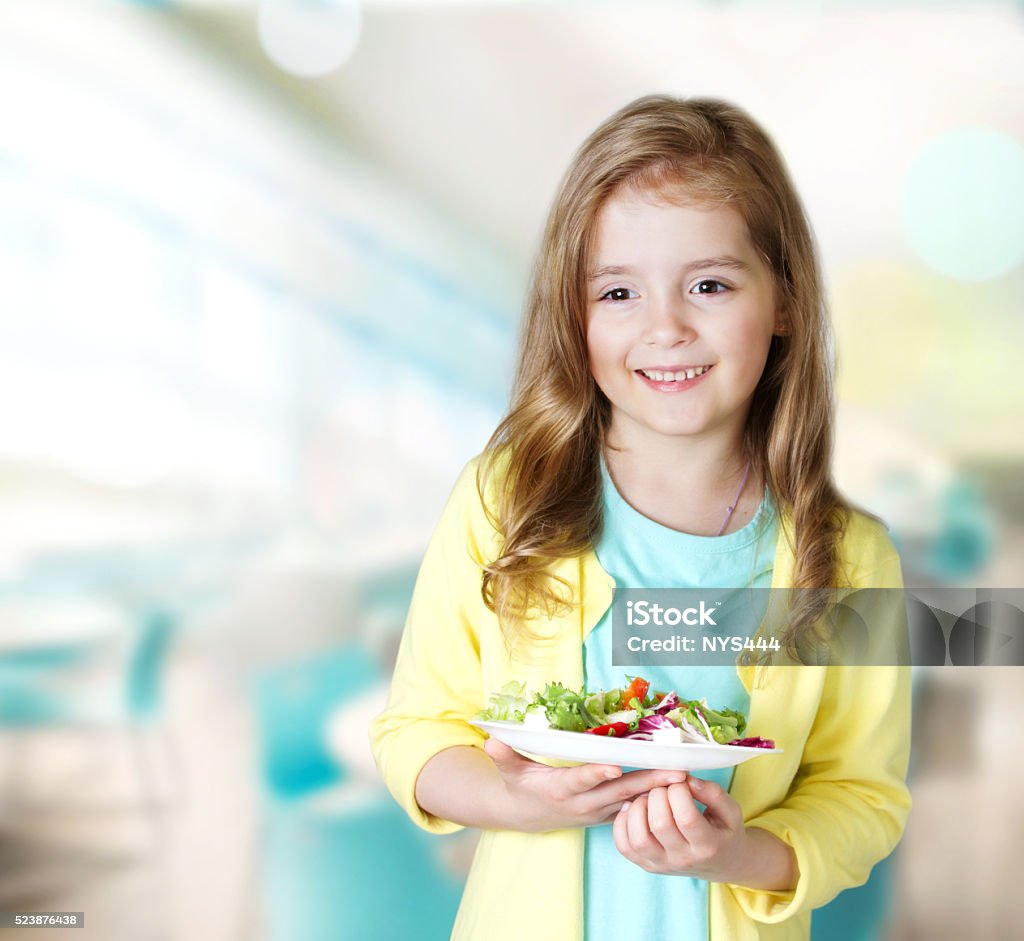 Child girl smiling carry plate salad in cafe background. Smiling child girl carry plate with fresh salad indoors school cafeteria dining room.Female caucasian kid healthy school nutrition concept background empty space. School Lunch Stock Photo