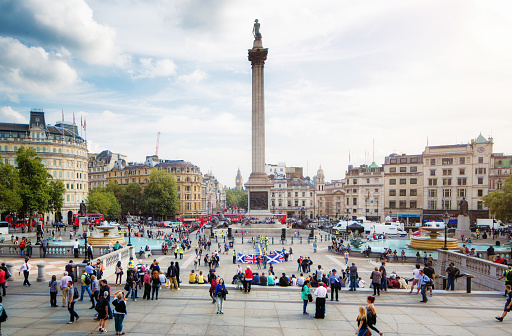 Busy Trafalgar Square London UK on sunny Autumn afternoon, with a nutrally occuring crowd of dozens of people, walking, sightseeing or relaxing around the monument.