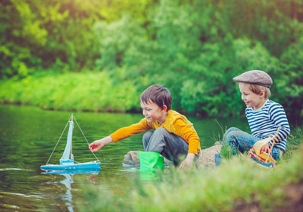 Little boys playing with their toy boat in a lake in spring