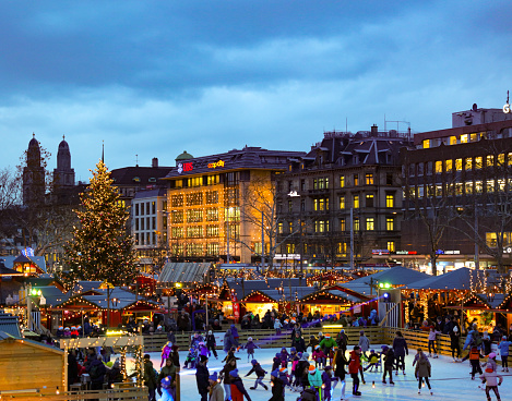 christmas market in zuerich at dawn. market huts and an icefield for iceskating. picture taken from the opera house in december 2015. In the background is the typical skyline of zuerich.
