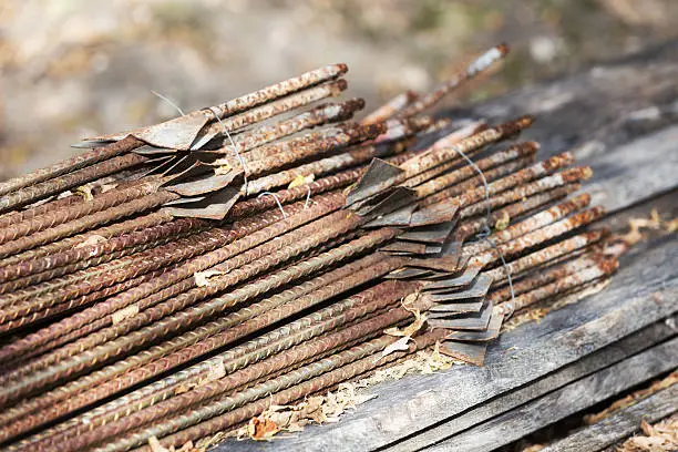 A pile of rusted rebar electric fenceposts on a stack of oak boards.