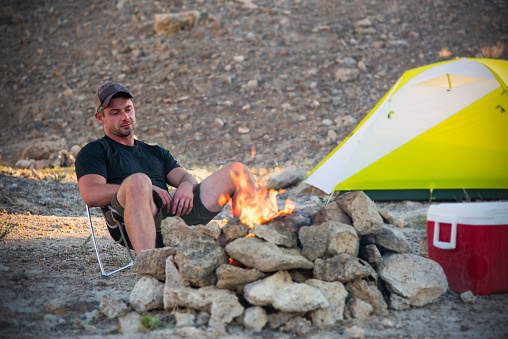 A 32 year old man relaxing by the campfire after a day in the wilderness hiking.  