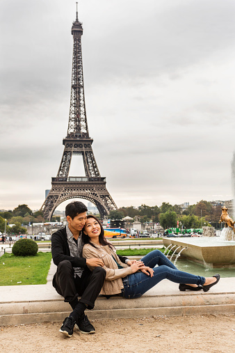 Romantic Asian couple relaxing by the Eiffel Tower while on vacation in Paris, France