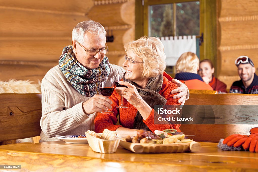 Senior couple having lunch after skiing, toasting wiht wine Senior couple wearing winter clothes sitting in a mountain restaurant after skiing, talking, enjoying dinner and drinking red wine.  Couple - Relationship Stock Photo